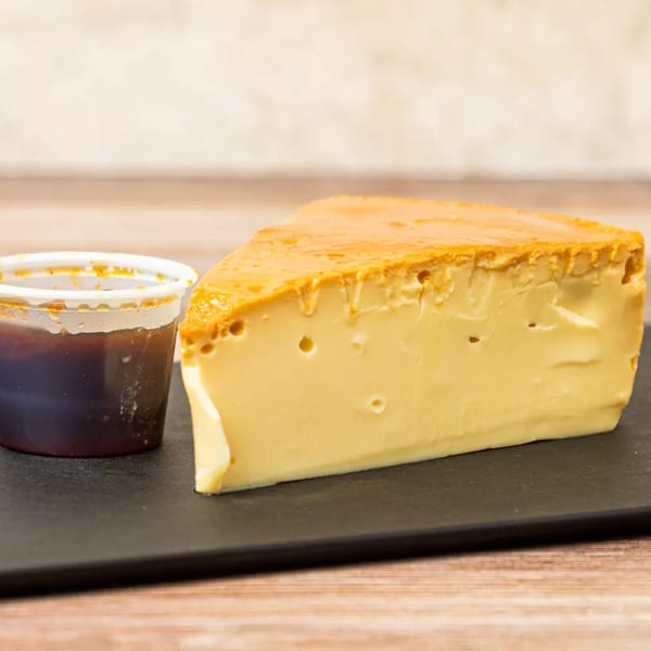 A slice of flan with caramel sauce on a black plate next to a small container of sauce.