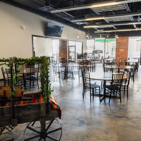 Spacious Chonchis Taco Shop dining room with round tables, black chairs, and a decorative wooden cart.