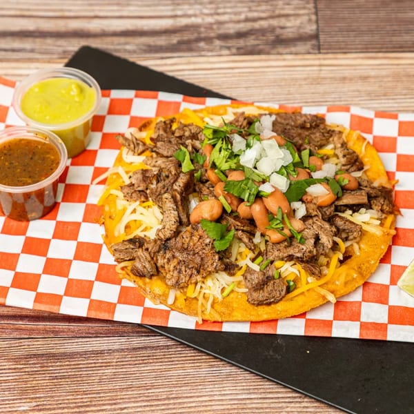 Chonchis Taco Shop's carne asada tostada with beans, onions, cilantro, and two sauces on a checkered paper.