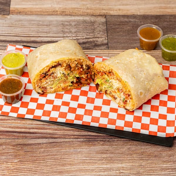 A large Chonchis Taco Shop burrito, cut in half, revealing its savory filling, with four salsa cups.