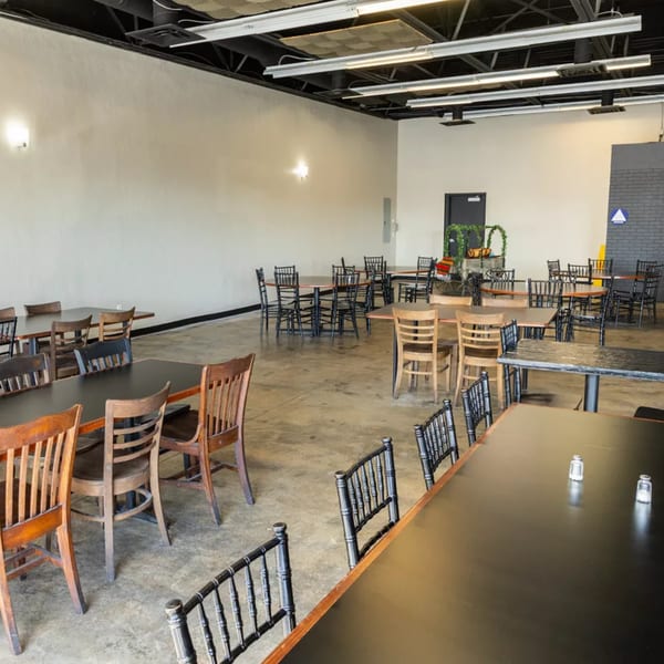 Spacious, empty dining room with numerous dark tables and a mix of wooden and black chairs.