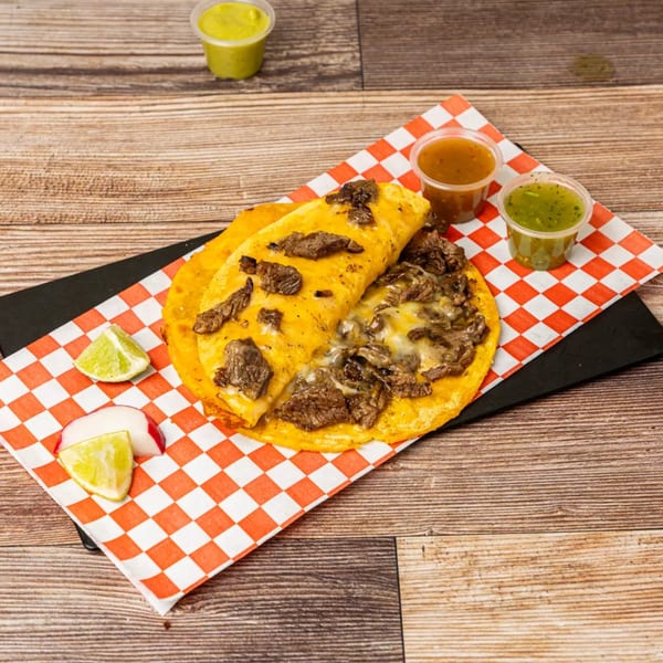 Chonchis Taco Shop's cheesy steak taco with lime, radish, and two sauces on a checkered paper.