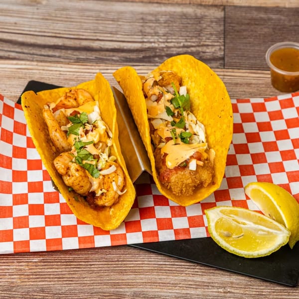 Two Chonchis Taco Shop tacos, one shrimp and one fish, with lemon wedges on a checkered paper.