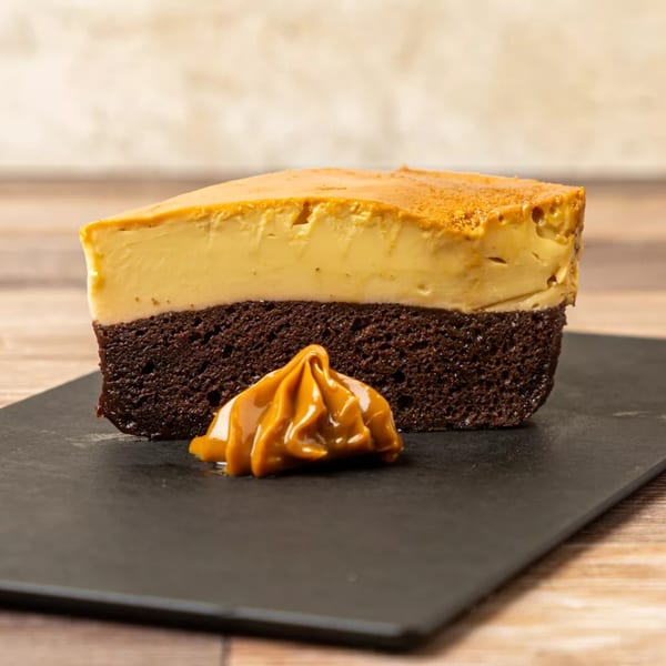 A slice of chocolate flan cake with a dollop of dulce de leche on a black plate.