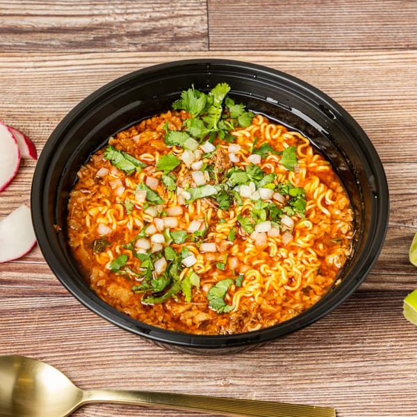 A black bowl of Chonchis Taco Shop ramen with cilantro and diced onions on a wooden table.